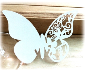 3D hollow paper butterfly place card with intricate floral cutout on light wood surface