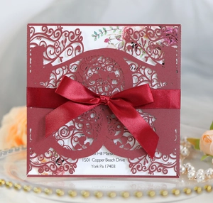 Detail of burgundy laser-cut wedding invitation featuring a ribbon bow and lace patterns