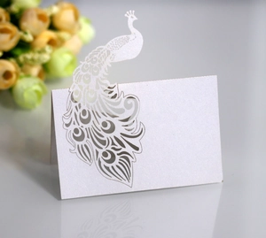 Macro shot of white pearlescent laser-cut peacock table card with elegant hollow pattern