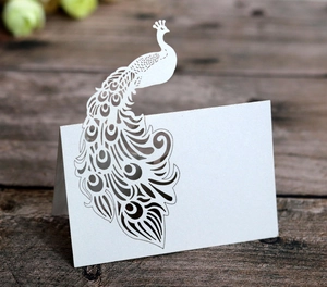 Macro detail of laser-cut peacock wedding place card made of white pearlescent paper