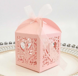 Detail view of pink laser-cut hollow wedding favor box with heart patterns and white ribbon