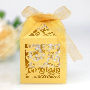 Detail of laser-cut gold wedding favor box with intricate bird motifs and ribbon