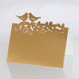 Détail d'un marque-place de mariage découpé au laser avec oiseaux dorés et feuilles