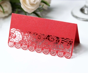 Macro detail of red laser-cut place card with lace floral patterns and glitter finish