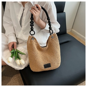 Detail of hand-woven straw bag featuring black polished bead handles and leather logo patch