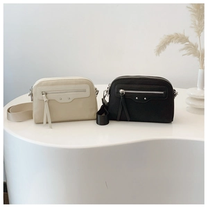Détail de sacs bandoulière minimalistes en beige et noir avec large sangle tissée