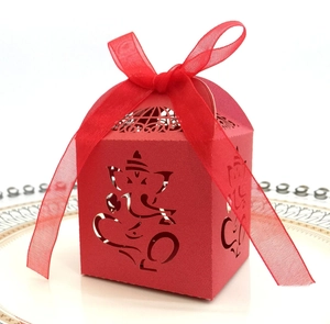 Macro detail of red laser-cut candy box featuring Ganesha motif and organza ribbon