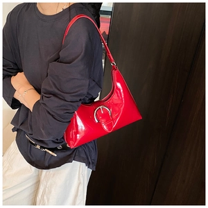 Detail of red patent leather underarm bag with glossy finish and large silver buckle