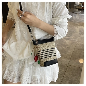 Detail of a beige straw bucket bag with black stripes and heart charms on a model