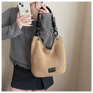 Detail of woven straw tote bag featuring black wooden bead handle and metal ring connector