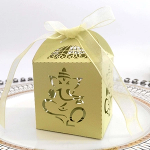 Detail of laser-cut Ganesha ivory favor box with white ribbon bow on elegant porcelain plate