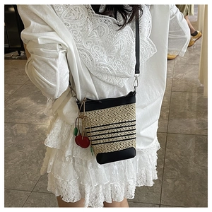 Detail of hand-woven straw bucket bag with black leather trim and cute cherry charm