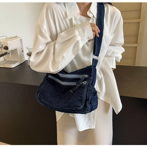 Macro detail of dark blue denim crossbody bag featuring multiple zipper pockets and texture