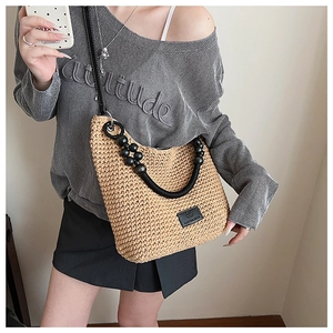 Model wearing a beige hollow woven crescent bag with black beaded handles and strap