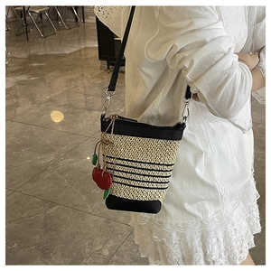Detail of a hand-woven straw bucket bag with black stripes and red cherry charms
