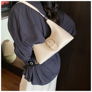 Detail of beige patent leather shoulder bag featuring a prominent silver round buckle
