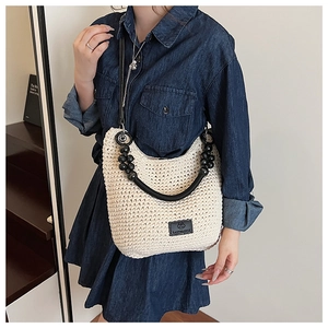 Close-up of beige woven bag featuring black beaded handle and branded leather patch