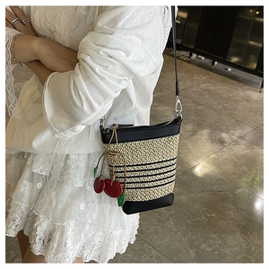 Detail of a beige woven bucket bag with black stripes and a red cherry charm on a model