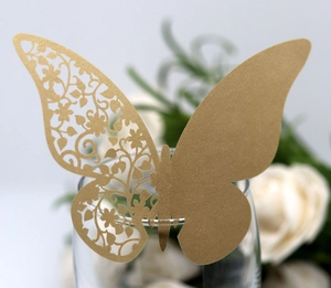Detailed laser-cut gold butterfly place card on a glass rim with floral background