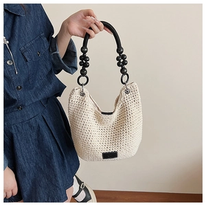 Detail of beige woven tote bag with black beaded handle and metallic ring attachment