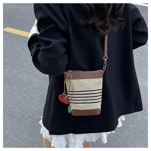 Close-up of beige straw woven crossbody bag with brown leather trim and cherry charm