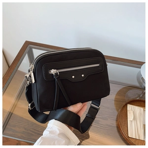 Détail du sac bandoulière en nylon noir avec double zip et large sangle sur table