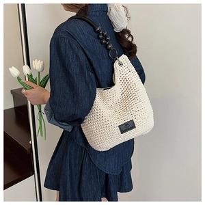 Detail of woven straw shoulder bag featuring unique black beaded strap and cream texture