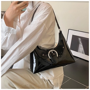 Detailed view of black patent leather underarm bag with a large silver circular metal buckle