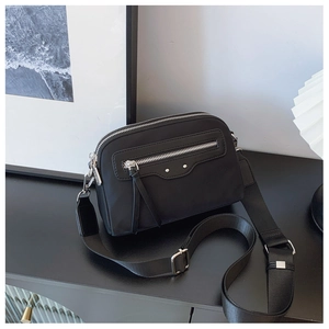 Détail d'un sac bandoulière en nylon noir avec double fermeture éclair et pompons
