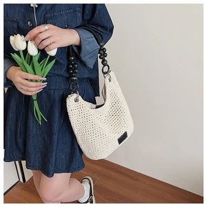 Detail of crochet hobo bag with contrast black beaded strap and brand label on cream fabric