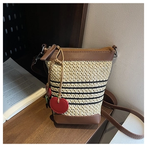 Detail of straw bucket bag with black stripes and red heart charm on wooden table