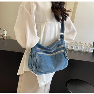 Detail of blue denim crossbody bag with multiple zippers and side elastic pockets