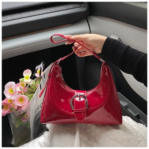 Detail of red patent leather hobo bag with large silver buckle in a car interior setting