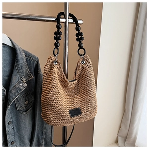 Detail of woven straw hobo bag featuring black beaded handle and metal strap buckle