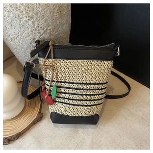 Close-up of woven straw bucket bag featuring black leather trim and cherry charm detail