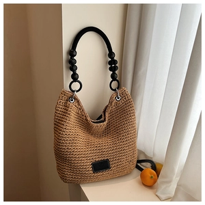 Close-up of woven straw shoulder bag featuring black beaded ring handle and leather detail