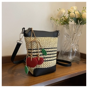 Detail of woven straw bucket bag with black leather trim and cute red cherry charm decoration