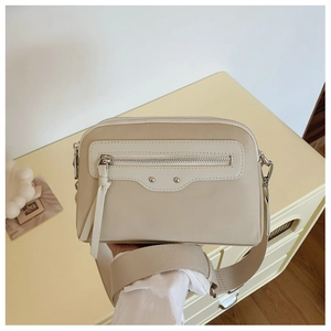 Détail du sac bandoulière en cuir crème avec sangle large et pompons zippés à franges