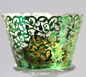 Close-up of laser-cut green metallic cupcake wrapper with intricate vine patterns