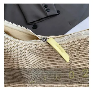 Dettaglio di una borsa tote in paglia color crema con cerniera in metallo e ricami gialli