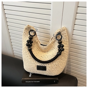 Close-up of beige crochet shoulder bag featuring black beaded handle and metal rings