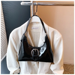 Detail of glossy black patent leather hobo bag with a silver buckle on a white blazer