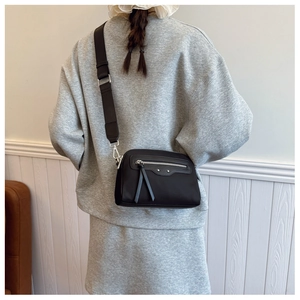 Détail de la large bandoulière réglable et des pompons sur le sac à bandoulière noir