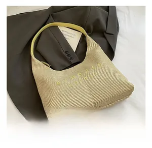 Dettaglio borsa hobo in paglia con manico in pelle gialla e ricamo del logo del brand