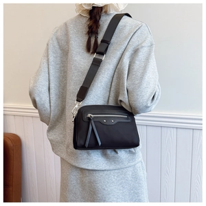 Détail du sac bandoulière en nylon noir avec large sangle et fermeture éclair argentée