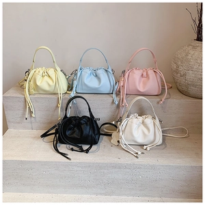 Collection of pleated drawstring bucket bags in five pastel colors on stone steps