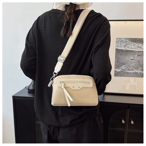 Sac bandoulière en nylon beige avec large sangle et détail de gland porté par une personne