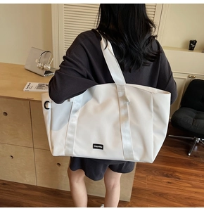 Detail view of a minimalist cream-white large tote bag with a woven brand tag and wide strap