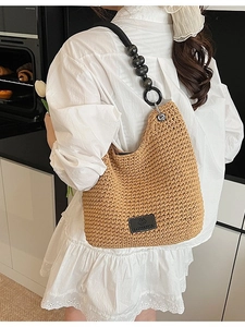 Straw woven shoulder bag with black beaded strap shown on a model in a long white dress