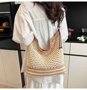 Detail of large woven tote bag with brown leather straps and striped bottom accents